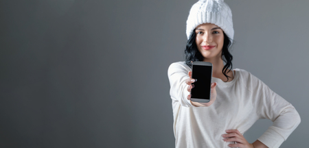 Young woman holding out a cellphone in her hand on a gray backgroundの写真素材