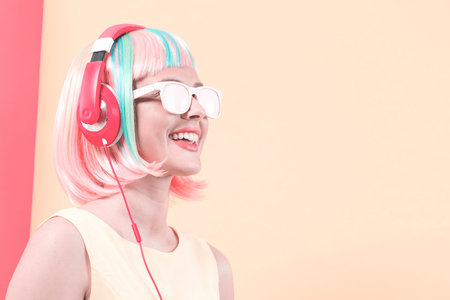 Woman in a colorful wig with headphones listening to music on a split yellow and pink backgroundの写真素材