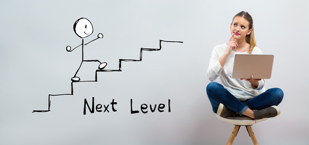 Next level concept with young woman using her laptop on a grey backgroundの写真素材