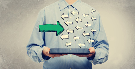 Arrow facing in a opposite direction with young man holding a tablet computerの写真素材