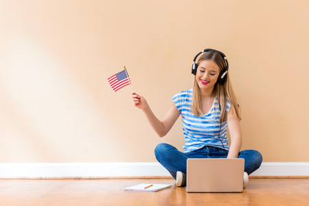 Young woman with USA flag using a laptop computer against a big interior wallの写真素材
