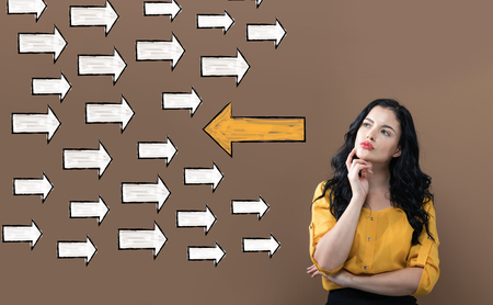 Arrow going in a opposite direction with young businesswoman on a brown backgroundの写真素材