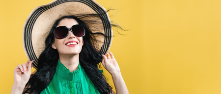 Young woman with a hat and sunglasses on a yellow background