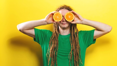 Happy young man holding oranges on a yellow background