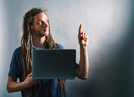 Young man pointing up while using a laptop on a dark backgroundの写真素材