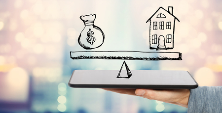 House and money on the scale with man holding a tablet computerの写真素材