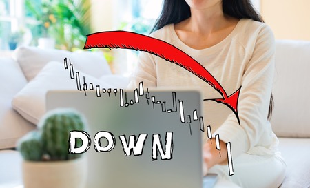 Market down trend chart with woman using her laptop in her home office