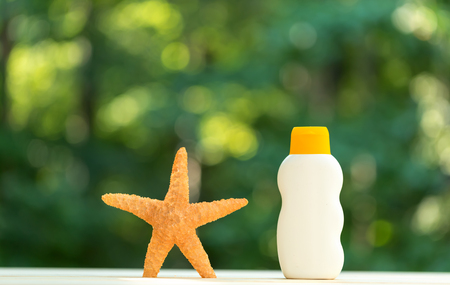 Bottle of sunblock and starfish on a shiny green forest backgroundの写真素材