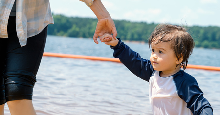 Toddler boy holding hands with his mother in a big lake on a summer dayの写真素材