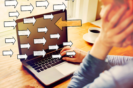 Arrow going in the opposite direction with man using a laptop computerの写真素材