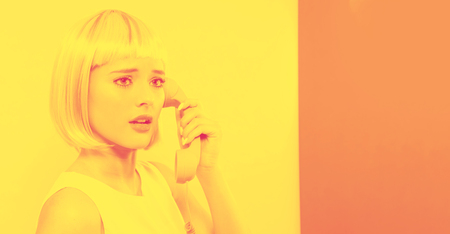 Young woman in a colorful wig talking on a retro phone on a split yellow and pink background with duotoneの写真素材