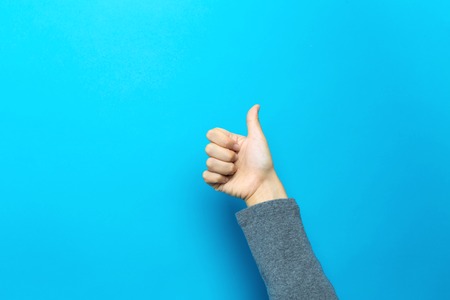 Person doing thumbs up gesture on a blue background