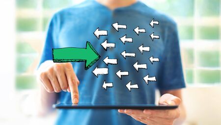 Arrow going in the opposite direction with young man using a tablet computerの写真素材