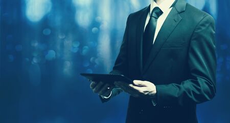 Businessman holding a tablet computer on a dark blue backgroundの写真素材