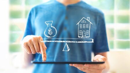 House and money on the scale with young man using a tablet computerの写真素材