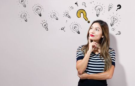 Question with light bulbs with young businesswoman in a thoughtful faceの写真素材