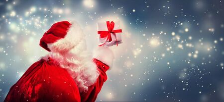 Santa holding a Christmas gift in snowy nightの写真素材