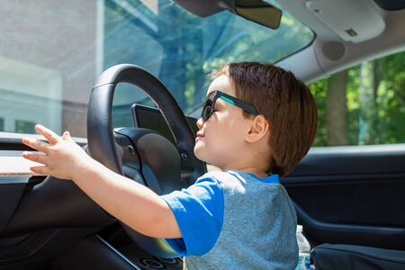 Toddler boy in playing in the driverss seat of his familys car in sunglassesの写真素材