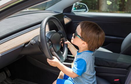Toddler boy in playing in the driverss seat of his familys car in sunglasses