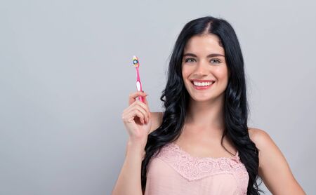 Young woman holding a toothbrush on a gray background