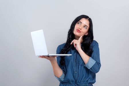 Young woman with a laptop computer in a thoughtful pose on a gray backgroundの写真素材
