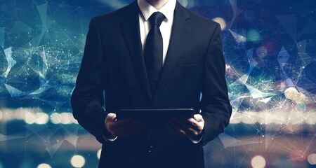 Businessman holding a tablet computer on night cityの写真素材