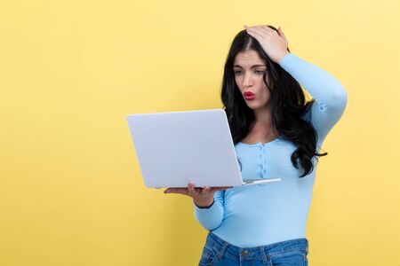 Surprised young woman using a laptop computer on a yellow background