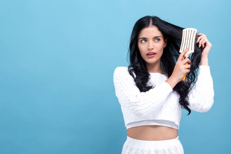 Beautiful young woman holding a hairbrush on a blue background