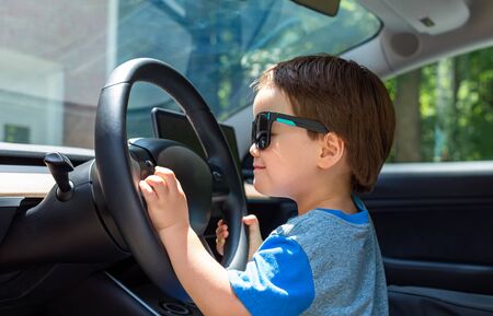 Toddler boy in playing in the driverss seat of his familys car in sunglassesの写真素材