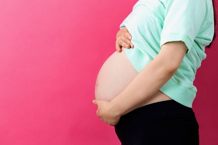 Pregnant woman on a solid background holding her bellyの写真素材