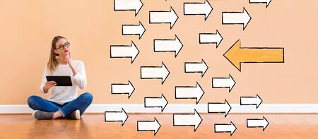 Arrow going in a opposite direction with young woman holding a tablet computerの写真素材