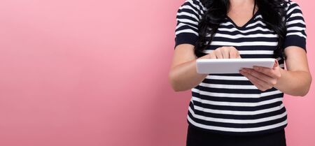 Young woman using her tablet on a pink backgroundの写真素材