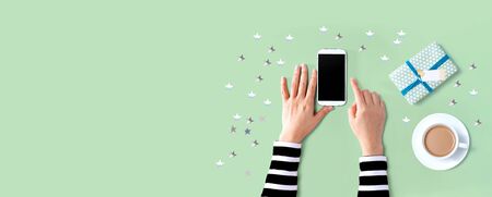 Person using a white smartphone with coffee and gift boxの写真素材