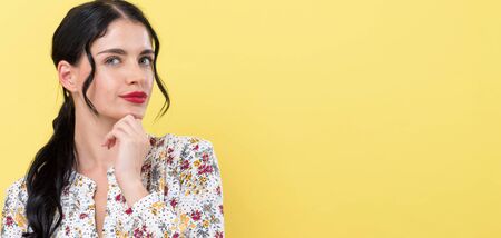 Young woman in a thoughtful pose on a yellow background