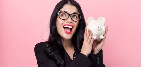 Young woman with a piggy bank on a pink backgroundの写真素材