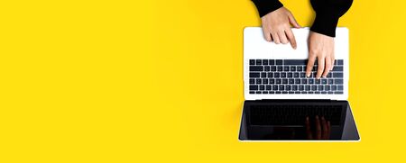 Person using a laptop computer on a solid color background