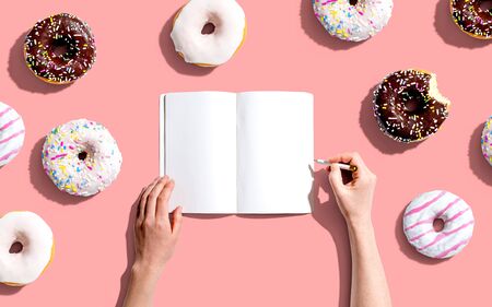 Person writing in a notebook with a collection of donutsの写真素材