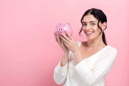 Young woman with a piggy bank on a pink backgroundの写真素材