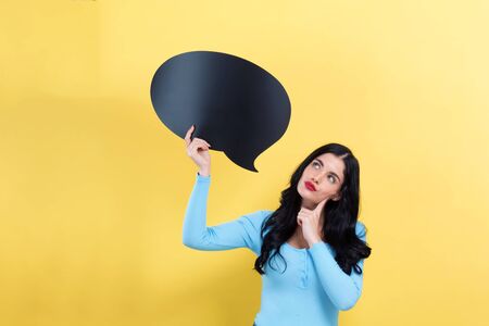 Young woman holding a speech bubble on a yellow backgroundの写真素材
