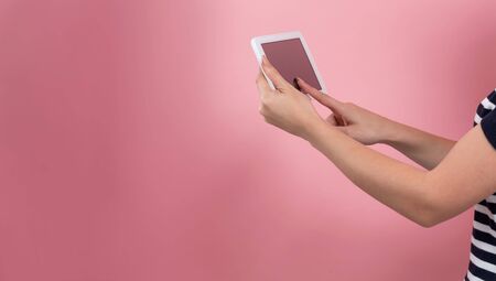 Young woman using her tablet on a pink backgroundの写真素材