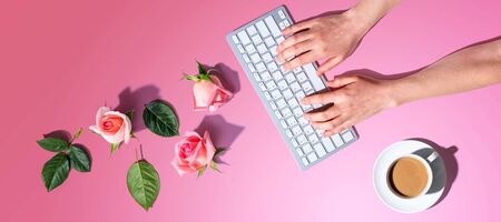 Woman using computer keyboard with pink roses - flat lay
