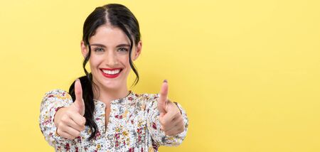 Young woman giving thumbs up on a yellow background