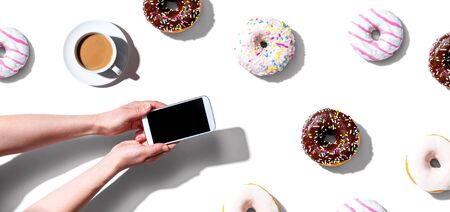 Person using a smartphone with donuts from aboveの写真素材