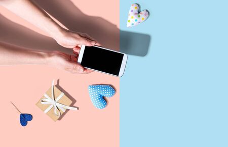 Woman holding her smartphone with small gift and heart cushions from above