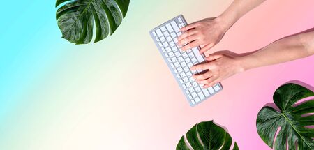 Person using a computer keyboard with tropical leaves from aboveの写真素材