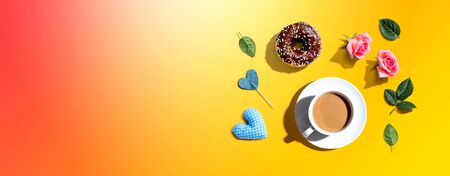 A cup of coffee with pink roses and a chocolate donut