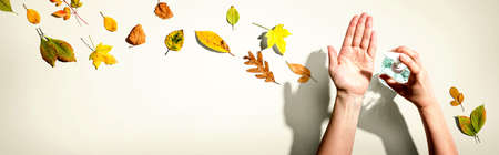 Applying sanitizer gel with autumn leaves - healthcare and hygiene conceptの写真素材