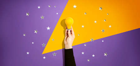 Person holding a yellow light bulb with silver shiny stars