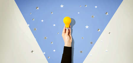 Person holding a yellow light bulb with silver shiny stars