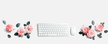 Computer keyboard and a mouse with pink roses - flat lay